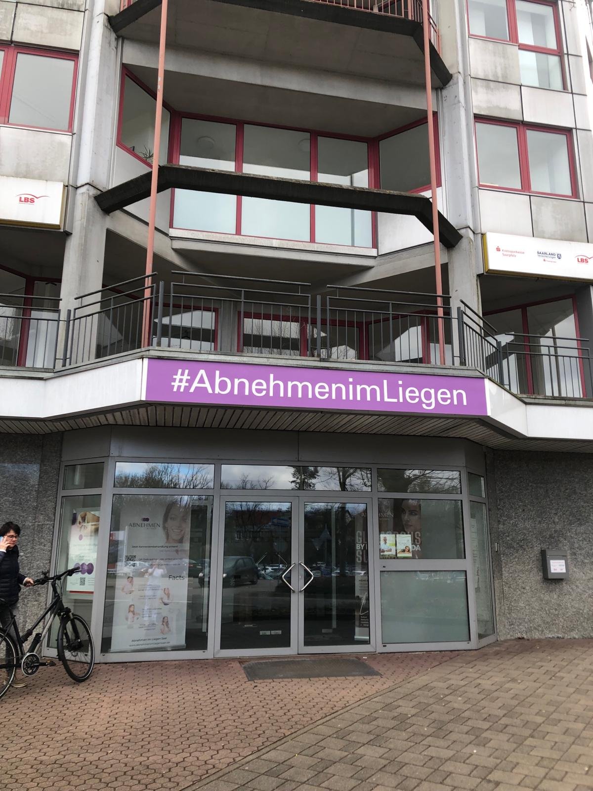 Eingang des Studios mit dem Schild #AbnehmenimLiegen an der Glasfassade