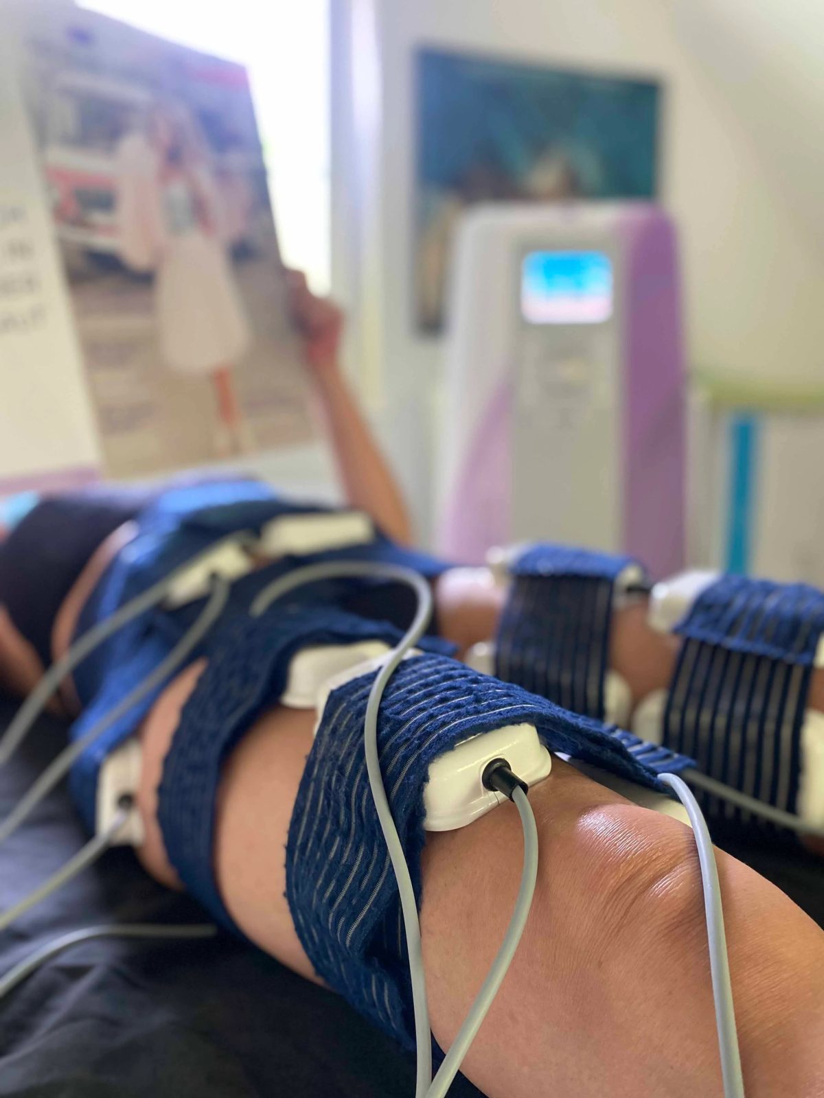 Kundin liegt auf der Behandlungsliege, an Bauch und Hüfte sind die Elektrodenmanschetten angelegt