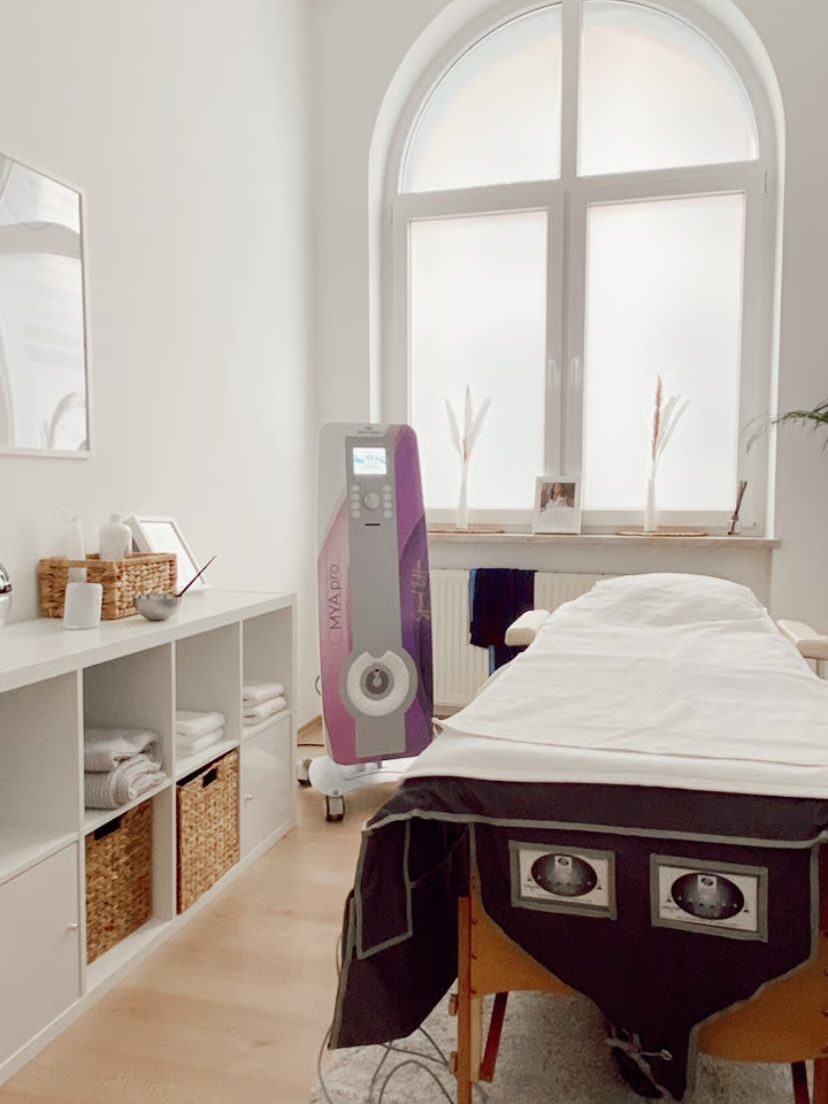 Behandlungsraum mit Bogenfenster, Liege und Regal mit Handtüchern