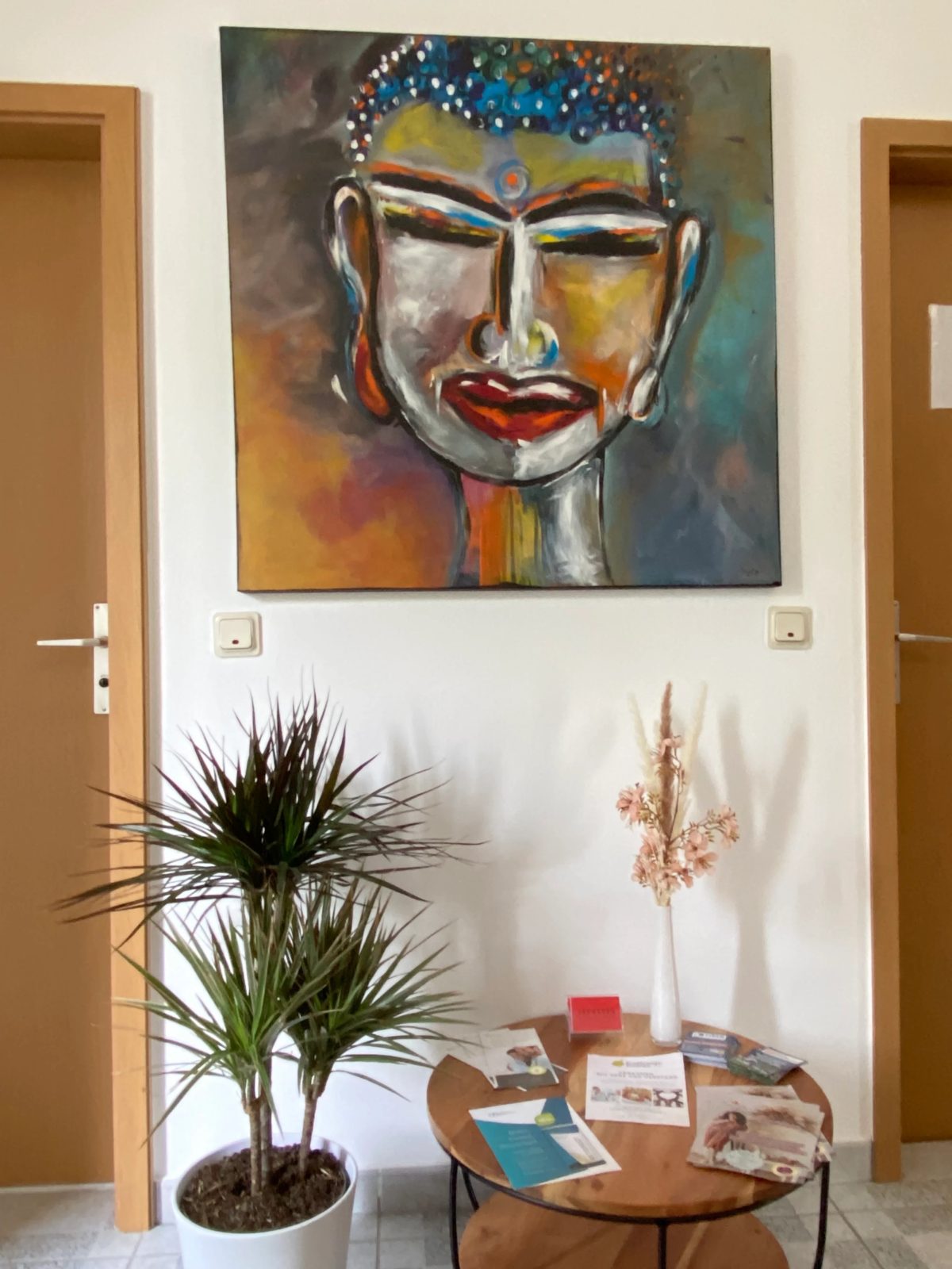 Wartebereich mit großem Buddha-Gemälde, Drachenbaum und Beistelltisch mit Prospekten